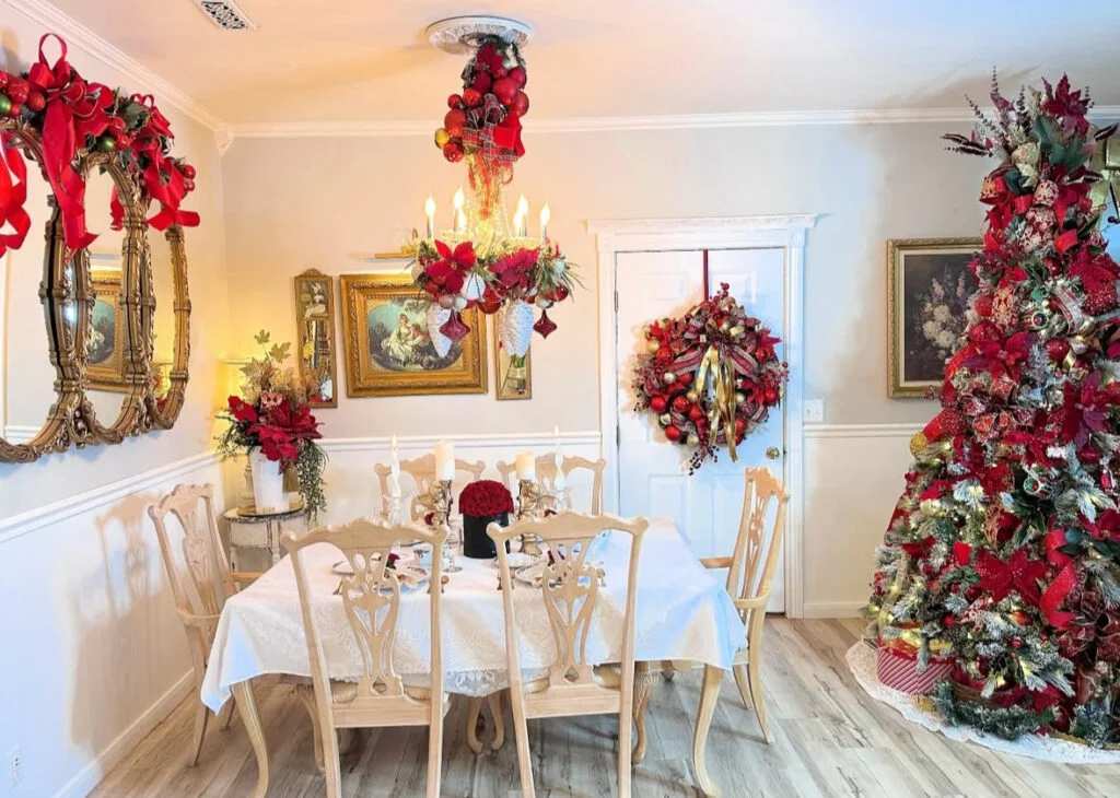 Formal dining room with a large wreath, red chairs, and a lit tree.