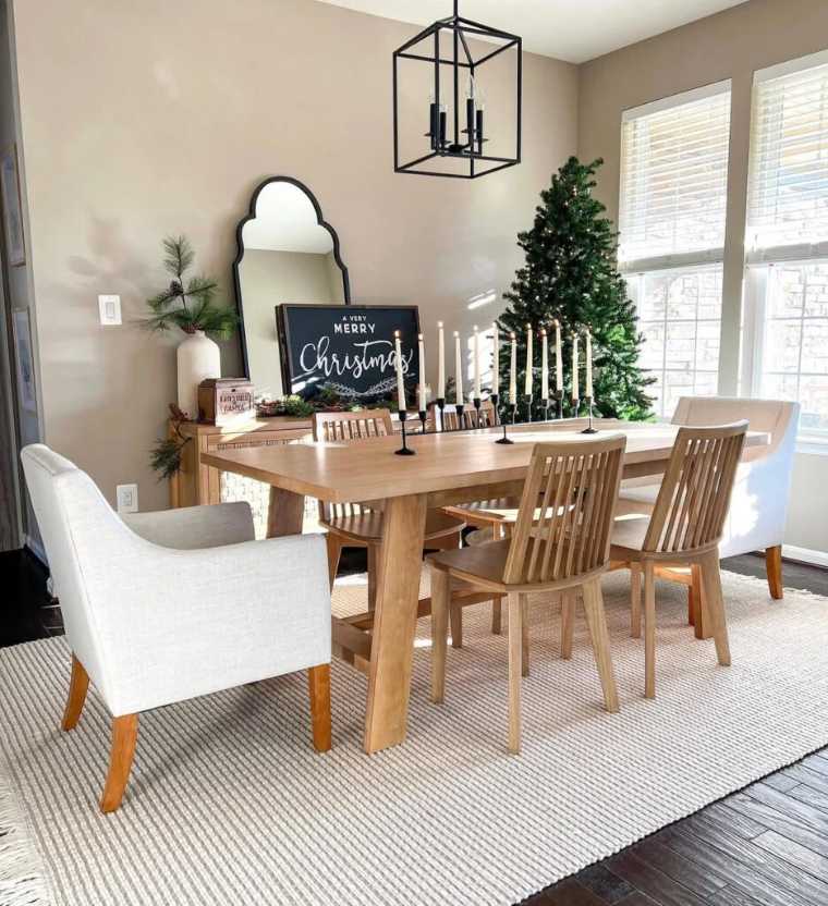 Light wood dining table with thin candlesticks and a Very Merry Christmas sign.
