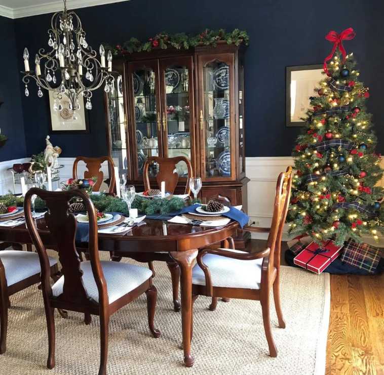 Dark navy dining room with a crystal chandelier, white tablecloth, and a lit Christmas tree.