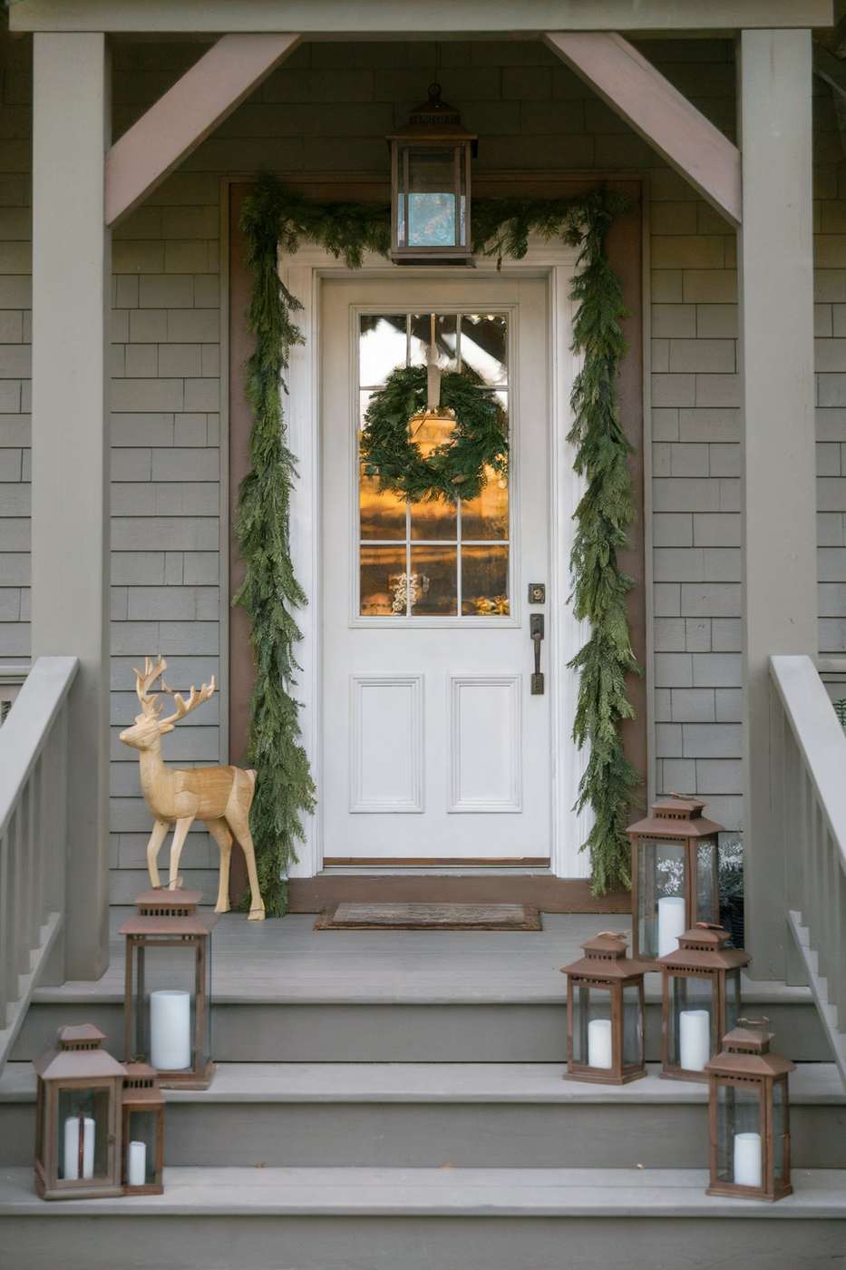 Modern front door featuring thin matte black hoop wreath decorated with sparse pine and flickering lanterns