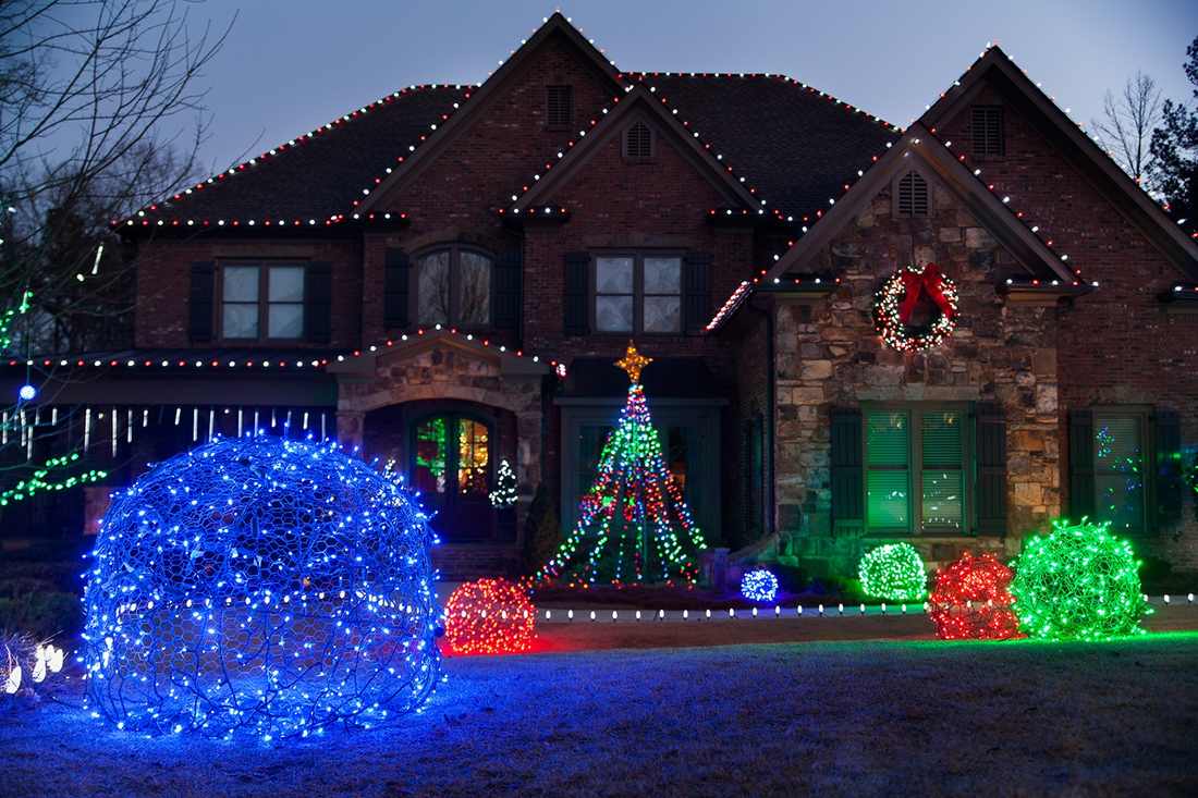 Spherical outdoor christmas decorations hanging from trees, glowing warm white light in yard.