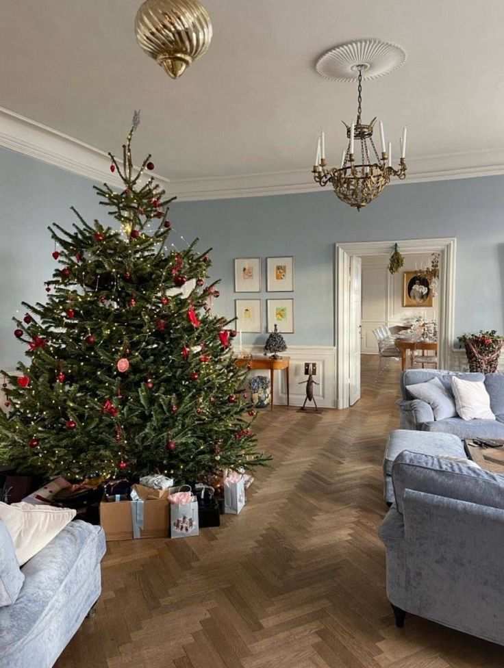 Large christmas tree with red ornaments in a blue room featuring a crystal chandelier.