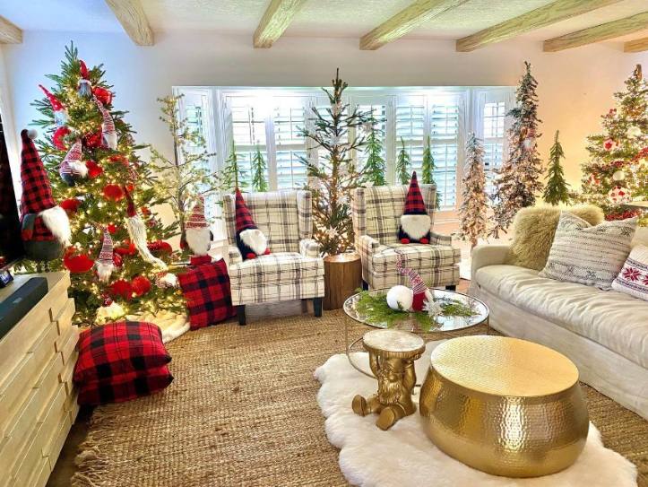 Red and black plaid pillows on a sofa with christmas gnomes and large trees in the background.