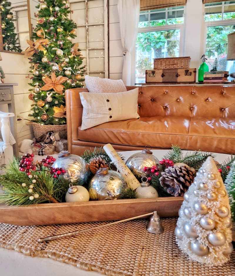 Living room fireplace hearth display with antique brass lanterns filled with iridescent silver ornaments and flickering candles.