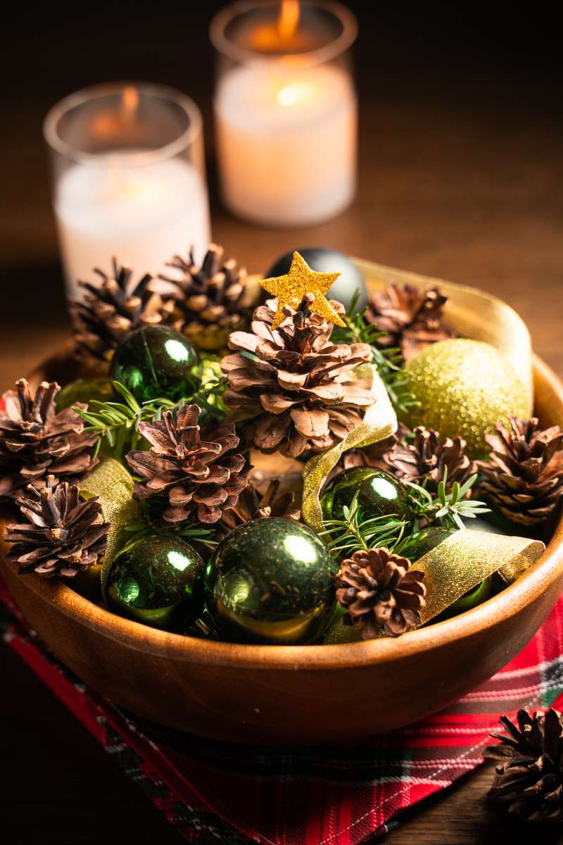 Stone fireplace mantel with rich green garland ornament display, velvet ribbon, warm incandescent glow.