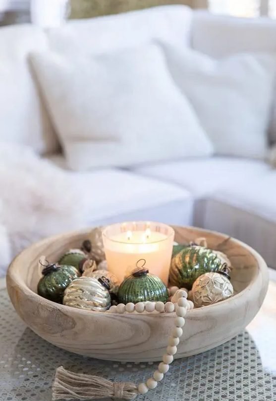 Rustic dining room table with dark clay bowl packed with matte brass ornaments under warm ambient lighting.