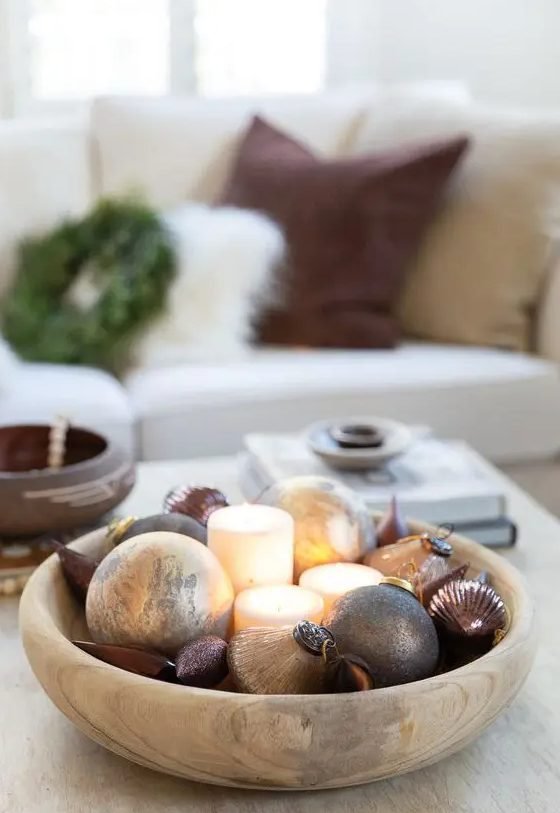 Cozy living room corner showing wooden ladder draped in evergreen garland hanging glass ornaments in warm light.
