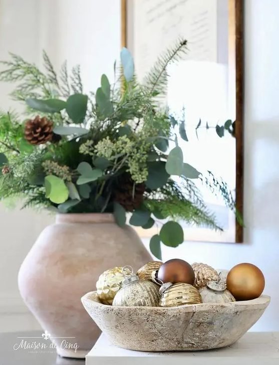 Luxurious living room fireplace mantel featuring gilded mirror draped with pine garland and oversized gold ornaments.