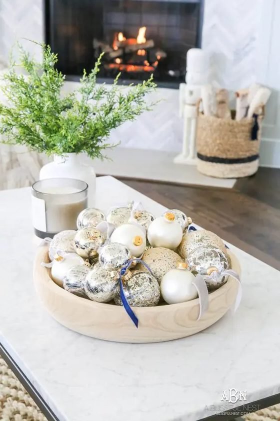 Coffee table with marble tray, assorted glass ornaments, pinecones, velvet pillows, neutral tones.