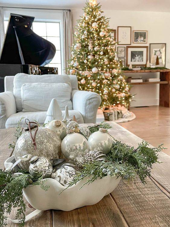 Console table with ceramic bowl, mixed holiday ornaments, neutral entryway, warm lamp lighting.