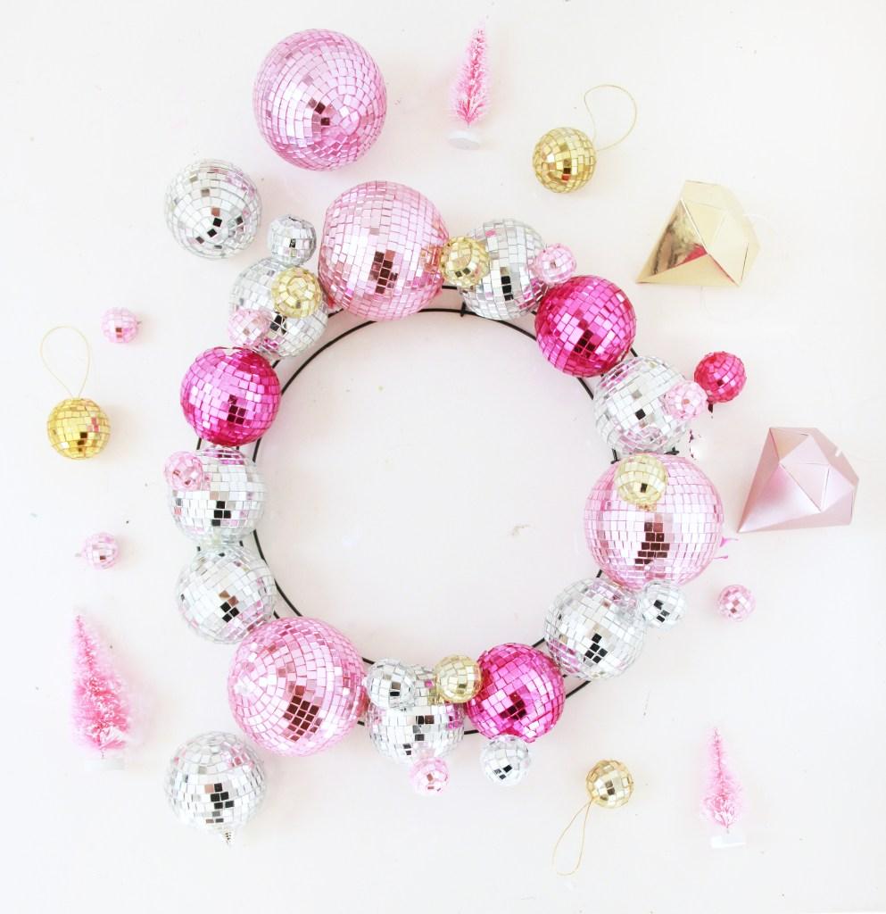 Pastel pink, lilac, and seafoam green christmas ornament wreath hanging on an antique white door with ambient light.