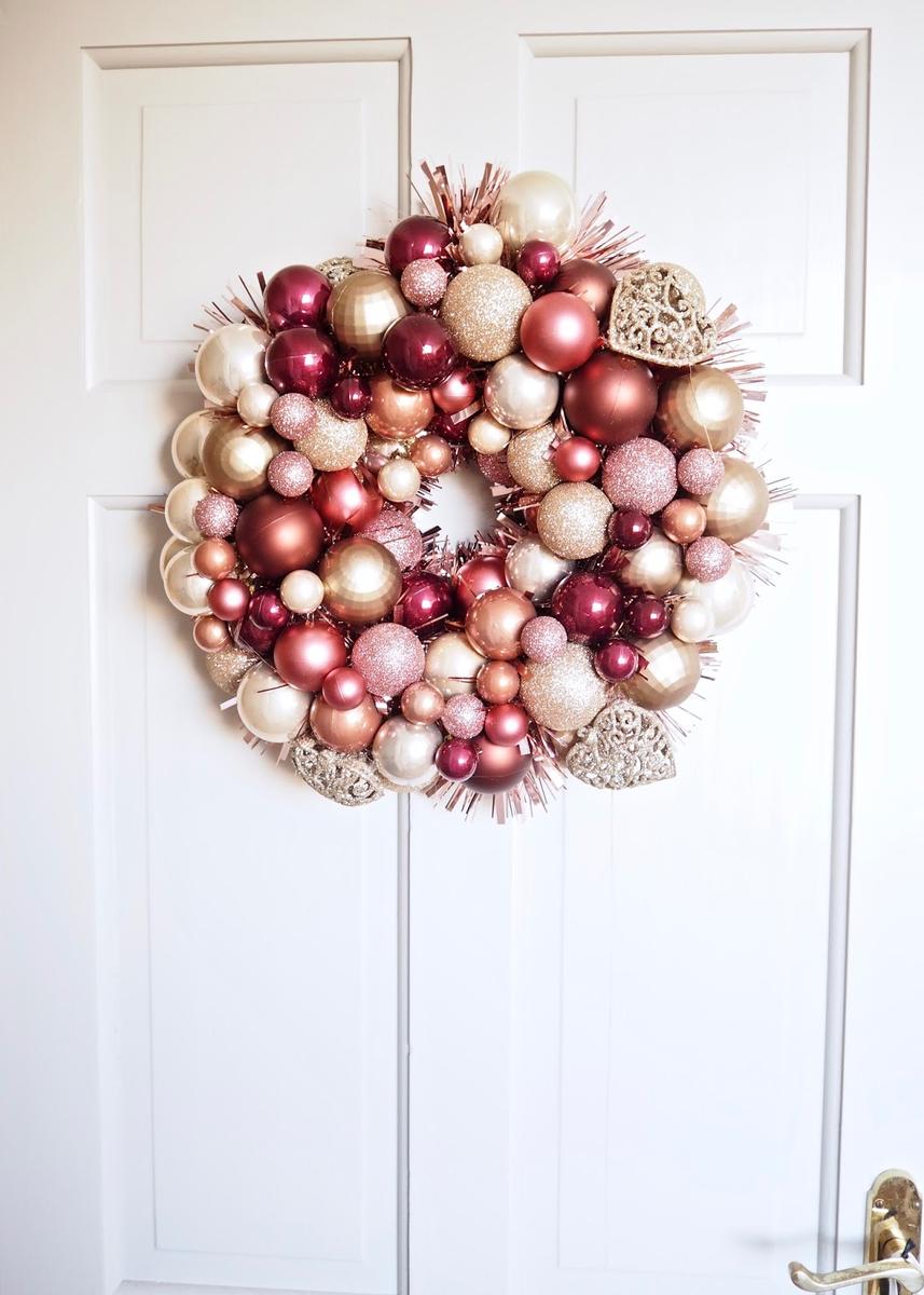 Deep navy blue and silver christmas ornament wreath displayed on a dark charcoal door under warm sconce light.