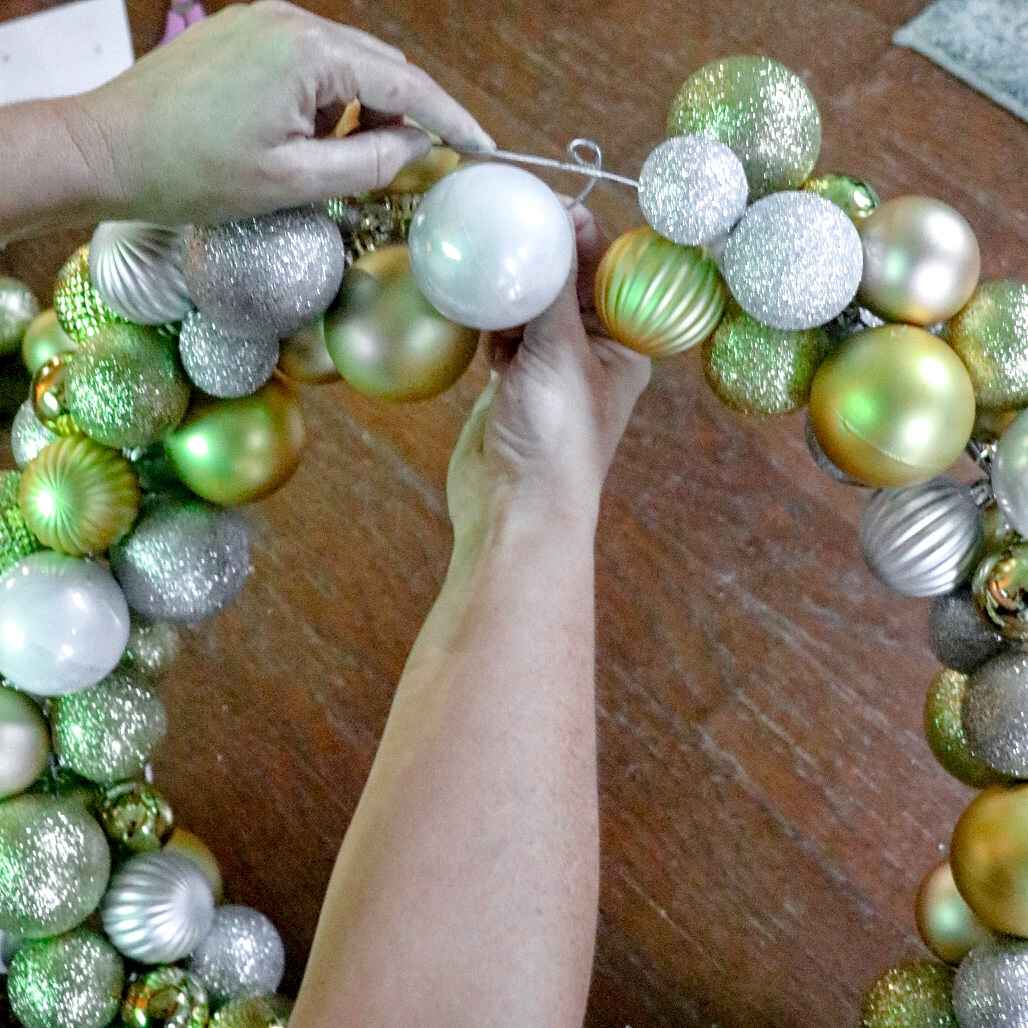 Flocked green fir wreath adorned with warm gold christmas ornaments and warm micro fairy lights on a wooden front door.