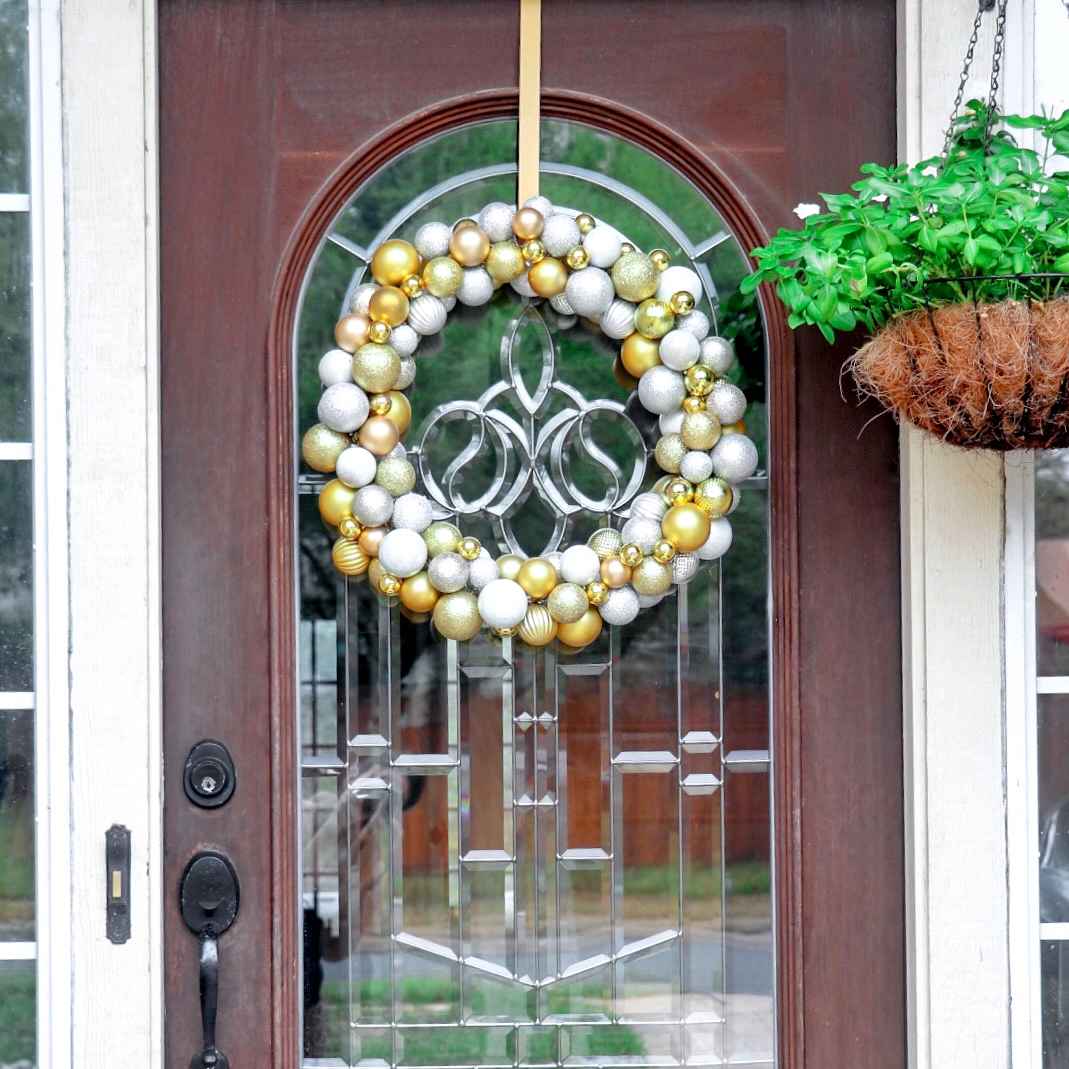 Traditional entry hall with dark walnut door, silver mercury glass ornament wreath, soft warm lantern lights.