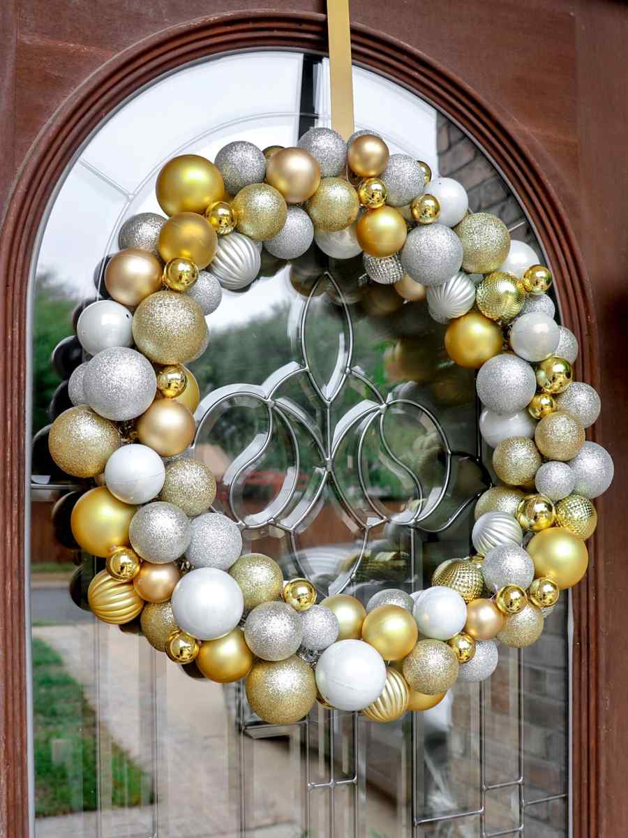 Glamorous dining room, navy door holding jewel-tone ornament wreath, brass accents, warm recessed lighting.