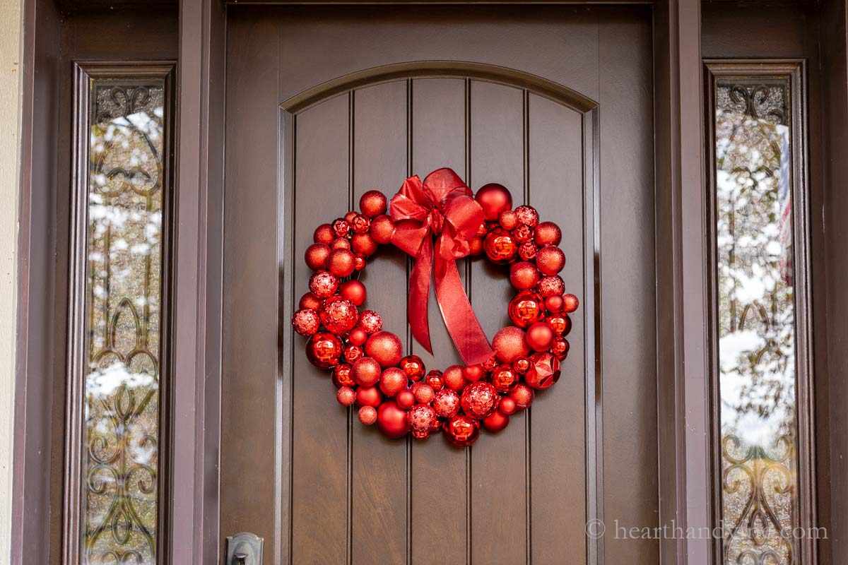 Calm mudroom, sage green ornament wreath, bench with linen cushions, soft natural warm window light.