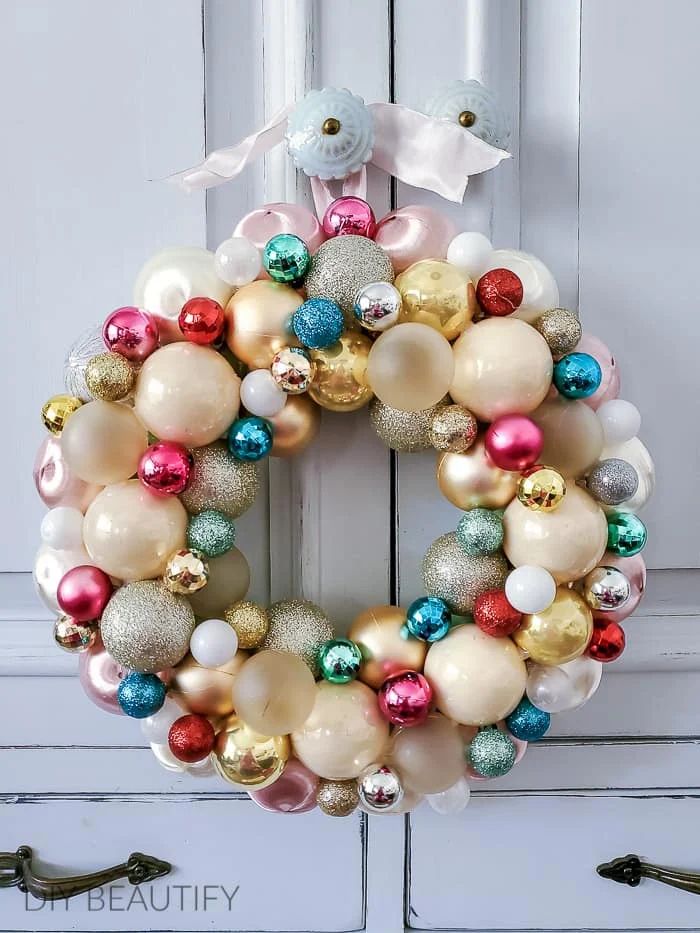 Silver and champagne christmas ornament wreath on a dark walnut door illuminated by warm sconces.
