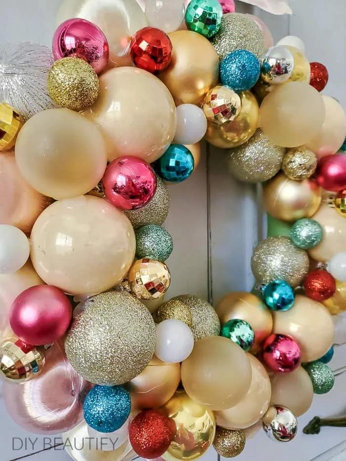 Pastel pink and mint green christmas ornament wreath on a white painted door in soft daylight.