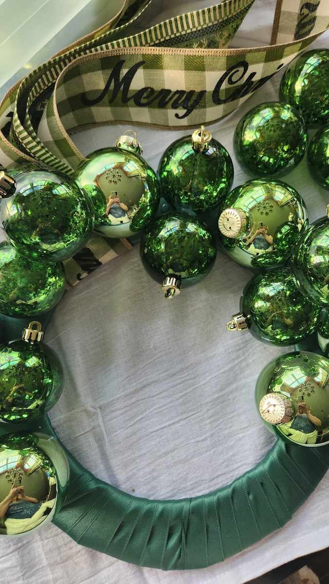 Crimson red and green christmas ornament wreath on a classic white door with warm wall sconces.