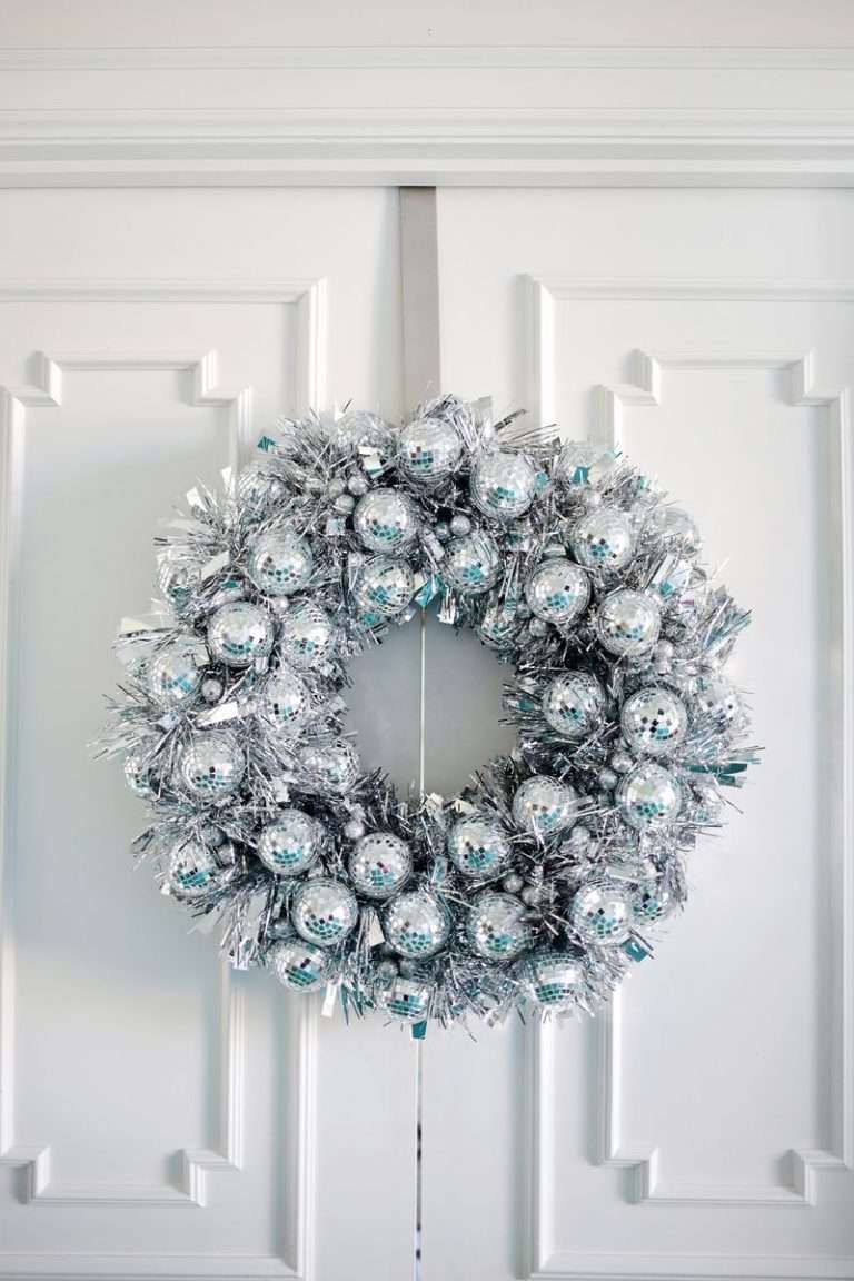 Minimalist brass ring christmas ornament wreath with matte cream balls on a natural pine door.