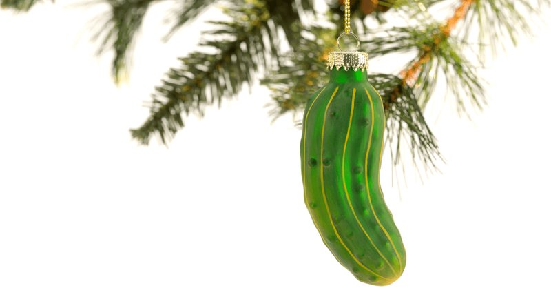 A glass cloche containing a small Christmas tree and a hidden pickle ornament.