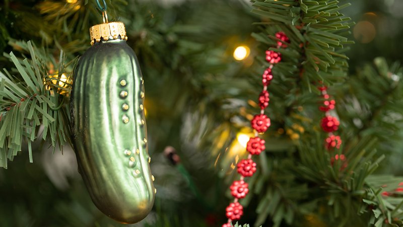 A wooden tray styled with plaid fabrics, pine, and a hidden pickle ornament.