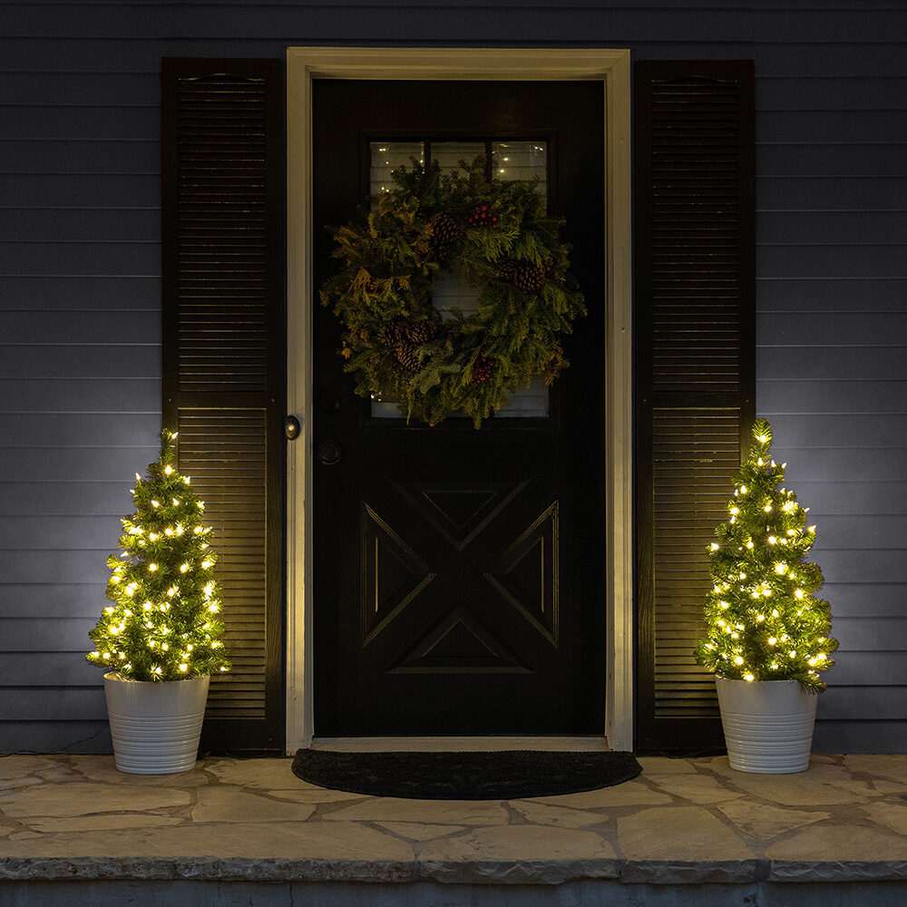 Front porch with twin potted evergreen trees decorated with subtle outdoor christmas decorations.
