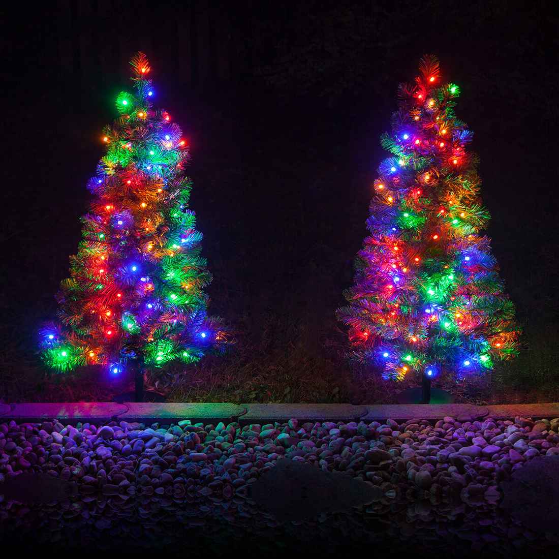 Pathway lined with mini pre-lit trees serving as festive outdoor christmas decorations.