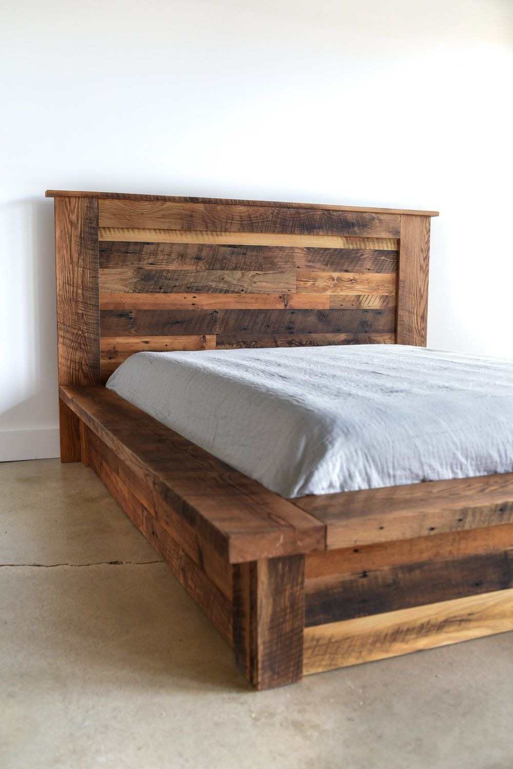 Rustic bedroom featuring a massive reclaimed wood bed frame, white linen bedding, and natural light from large windows