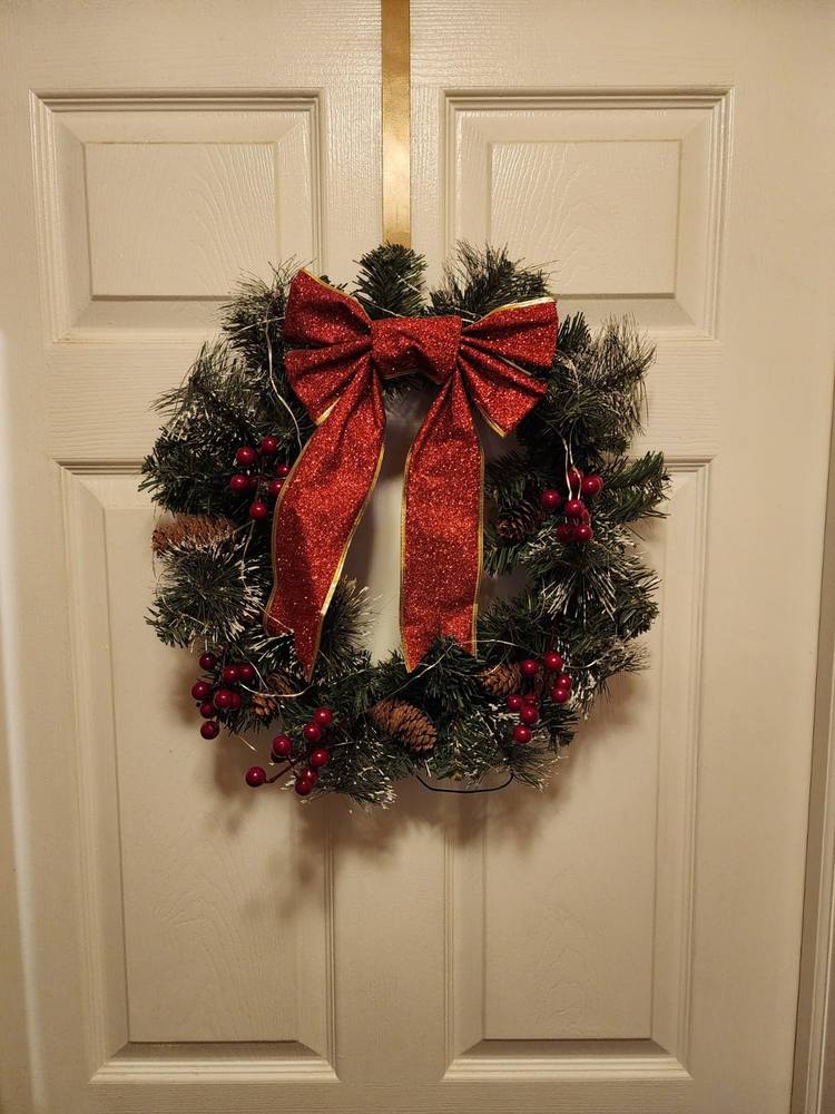 Traditional front porch displaying rich green pine wreath topped with large glittery red bow.