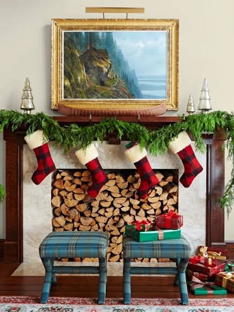 Traditional colonial living room with lush pine garland, mahogany millwork, red stockings, and warm firelight.