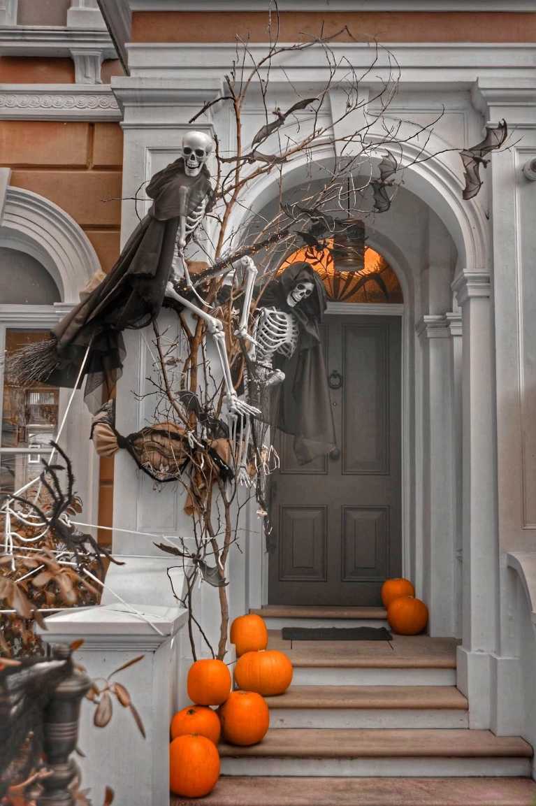 Cloaked skeletons climbing a tree next to an arched entryway on a porch.