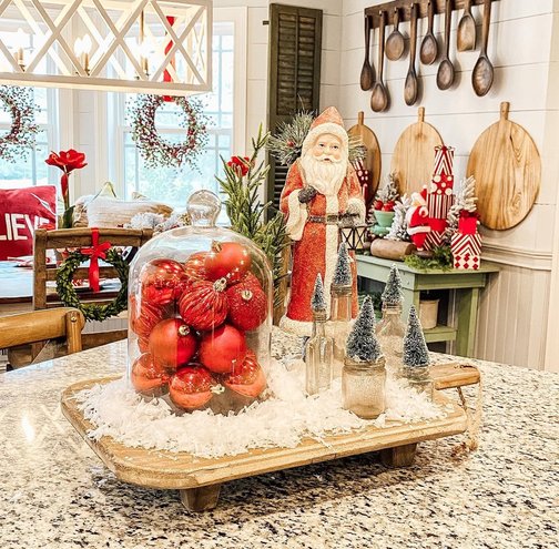 Glass cloche containing mini Santa and snow scene on wooden kitchen shelf.