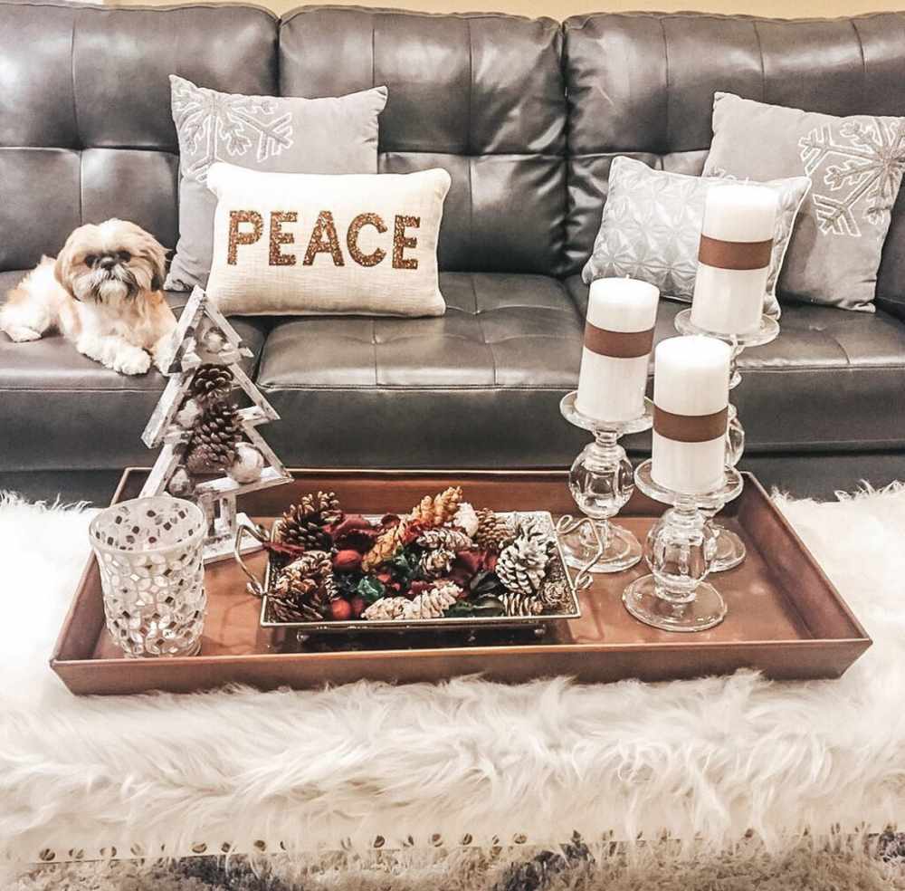 Hammered copper tray holding various sizes of metallic candle holders on a dark coffee table.