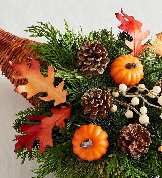 Close‑up view, wooden table, pinecone cornucopia, evergreen sprigs, orange pumpkin, soft side lighting.