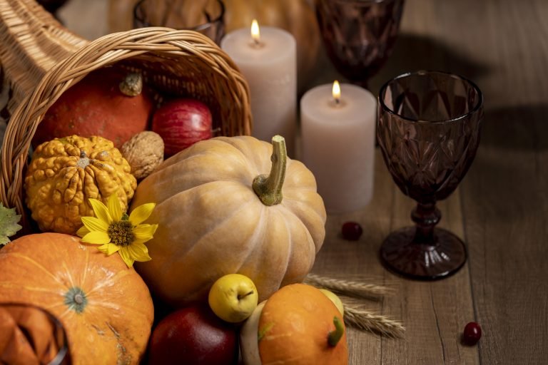Close‑up on tabletop, pumpkin cornucopia, sunflowers, tealight candles, warm backlighting.