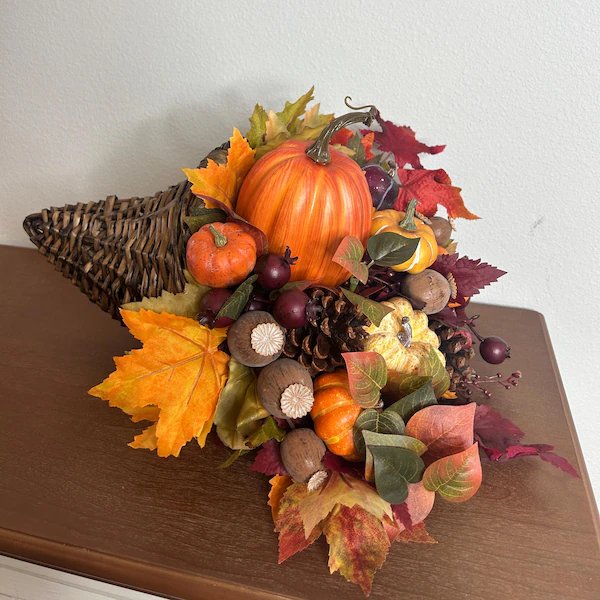 Living room side table, orange pumpkin cornucopia, pinecones, metal stand, diffused natural light.