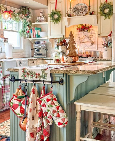 Fresh holly branches and berries in a ceramic bowl on a white kitchen island.