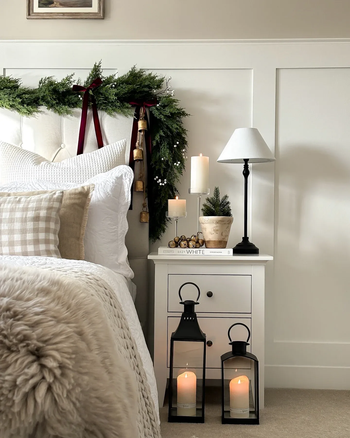 Intimate bed nook decorated with green garland, lit pillar candles, plush blankets, and warm ambient lighting.
