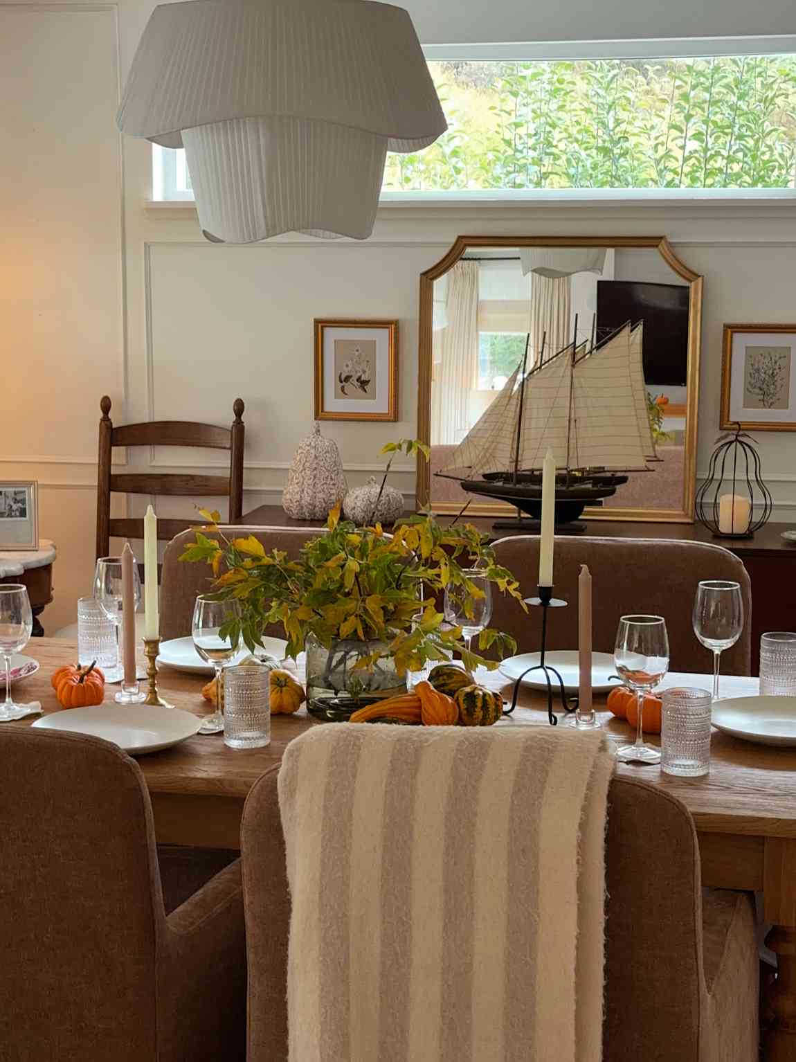 Intimate dining room, mini pumpkins, tealight candles, autumn branches, soft warm lighting, wooden chairs.