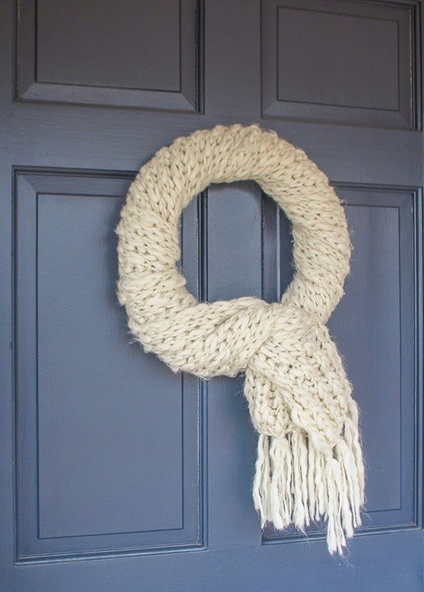 Mustard yellow cable knit scarf wreath hanging on a navy blue painted wood entryway door