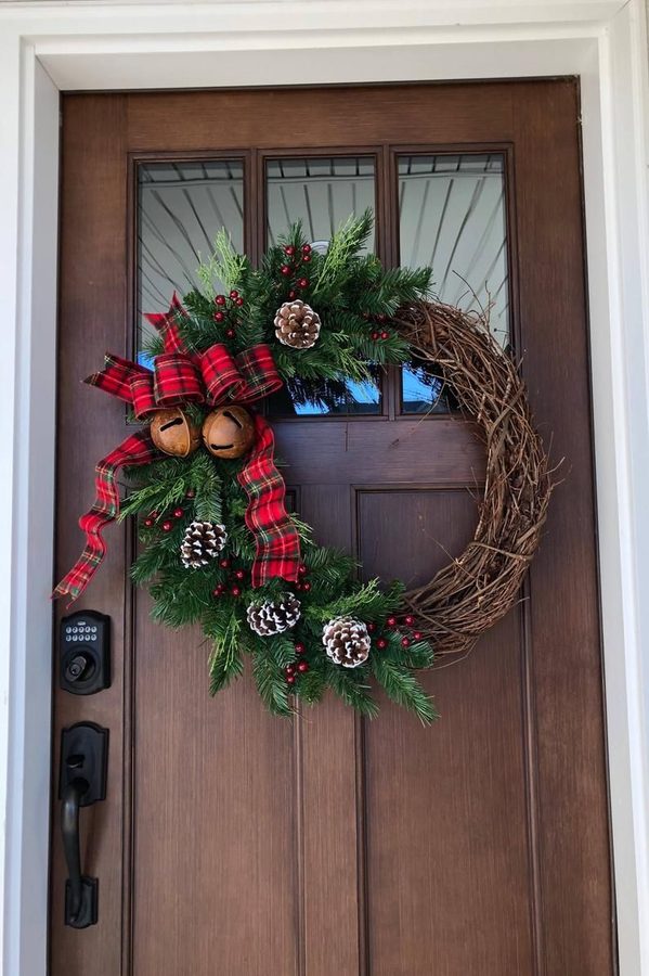 Red plaid scarf wreath displayed above white brick fireplace mantel illuminated by soft candle glow.