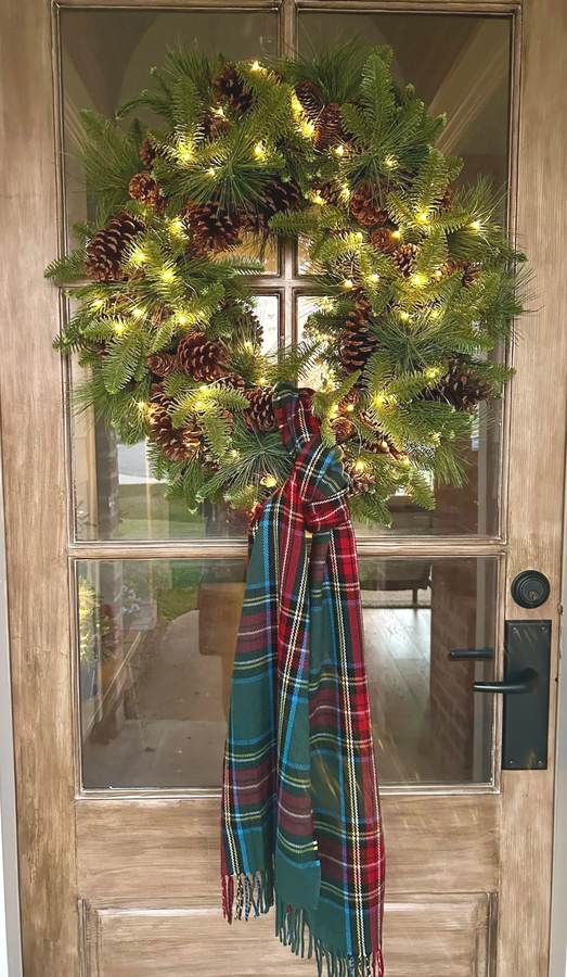 Light gray cashmere scarf wreath with hanging tassels on light wood dining room wall.