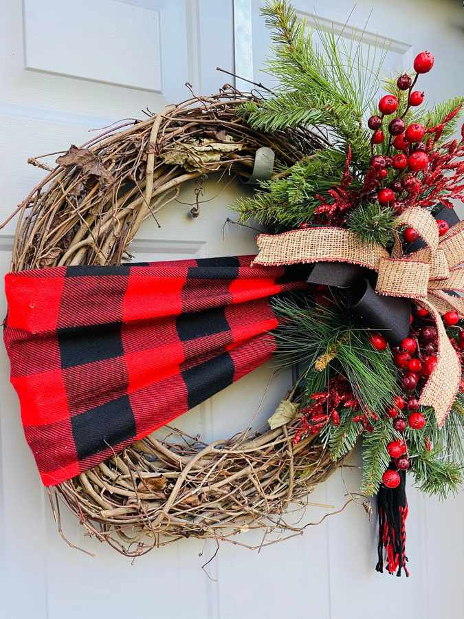 Red plaid wool scarf wreath hanging on mudroom coat hooks with bench and warm lantern light