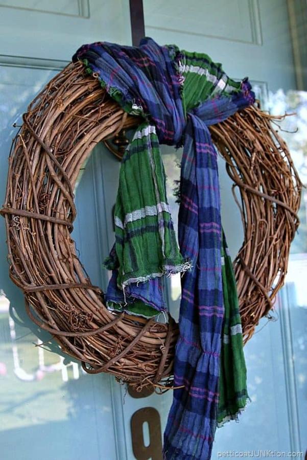 Deep emerald velvet wrapped scarf wreath above upholstered bedroom headboard under soft golden sconce lighting