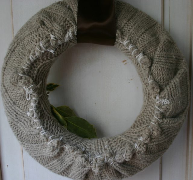 Cozy reading nook featuring hunter green cable-knit scarf wreath above leather armchair and wooden shelf.