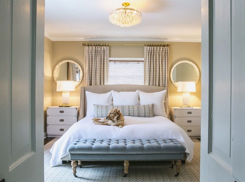 Cozy master bedroom featuring a blue tufted bench and decorative round mirrors