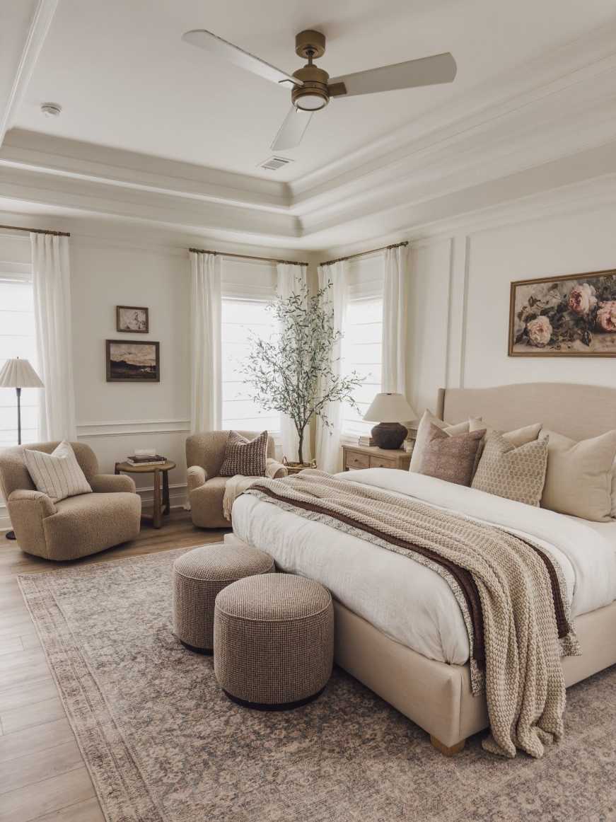 Spacious neutral master suite with a dedicated seating nook and plush ottomans