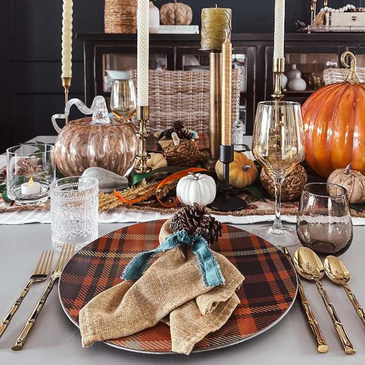 Place setting with plaid napkins, brushed copper flatware, textured ceramic plates, warm candlelight