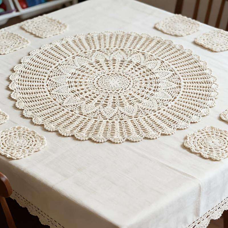 Dining room table with crochet lace runner, wooden chairs, white linen, warm yellow lighting.